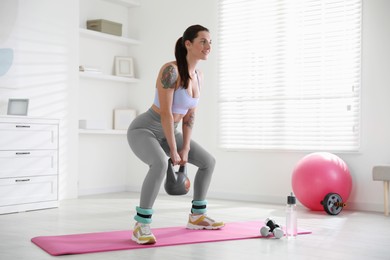 Beautiful woman with ankle weights and kettlebell training indoors