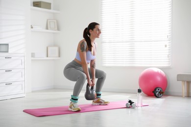 Beautiful woman with ankle weights and kettlebell training indoors