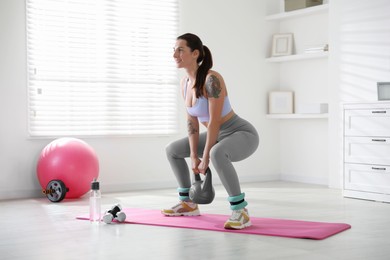 Photo of Beautiful woman with ankle weights and kettlebell training indoors