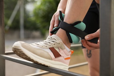 Photo of Woman putting on ankle weight outdoors, closeup