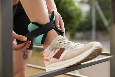 Photo of Woman putting on ankle weight outdoors, closeup