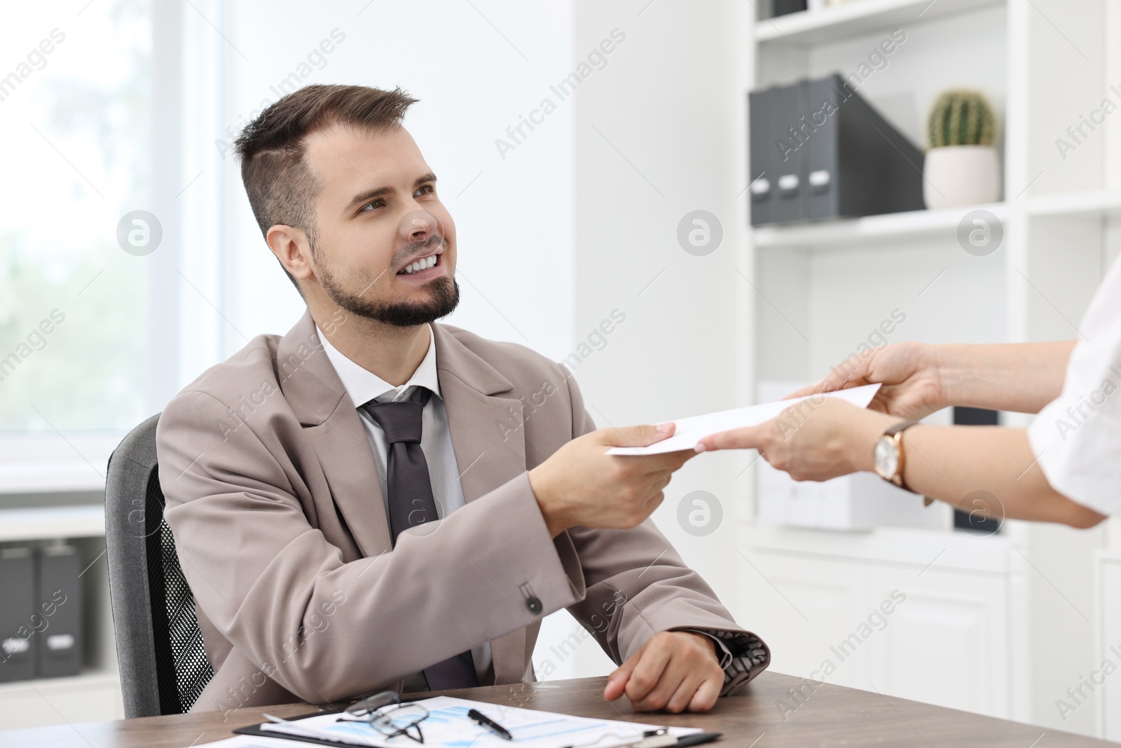 Photo of Smiling employee receiving envelope with salary from boss in office