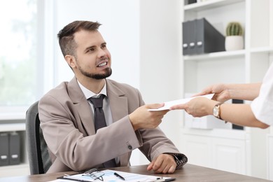 Smiling employee receiving envelope with salary from boss in office