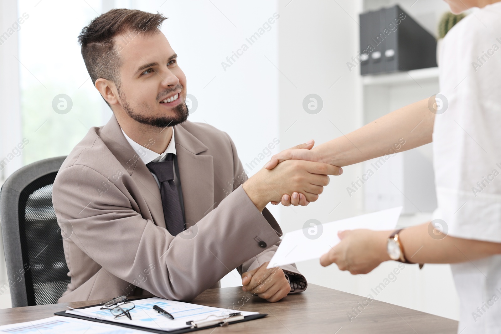 Photo of Smiling employee shaking hands with boss while receiving envelope with salary in office