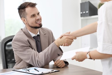 Smiling employee shaking hands with boss while receiving envelope with salary in office