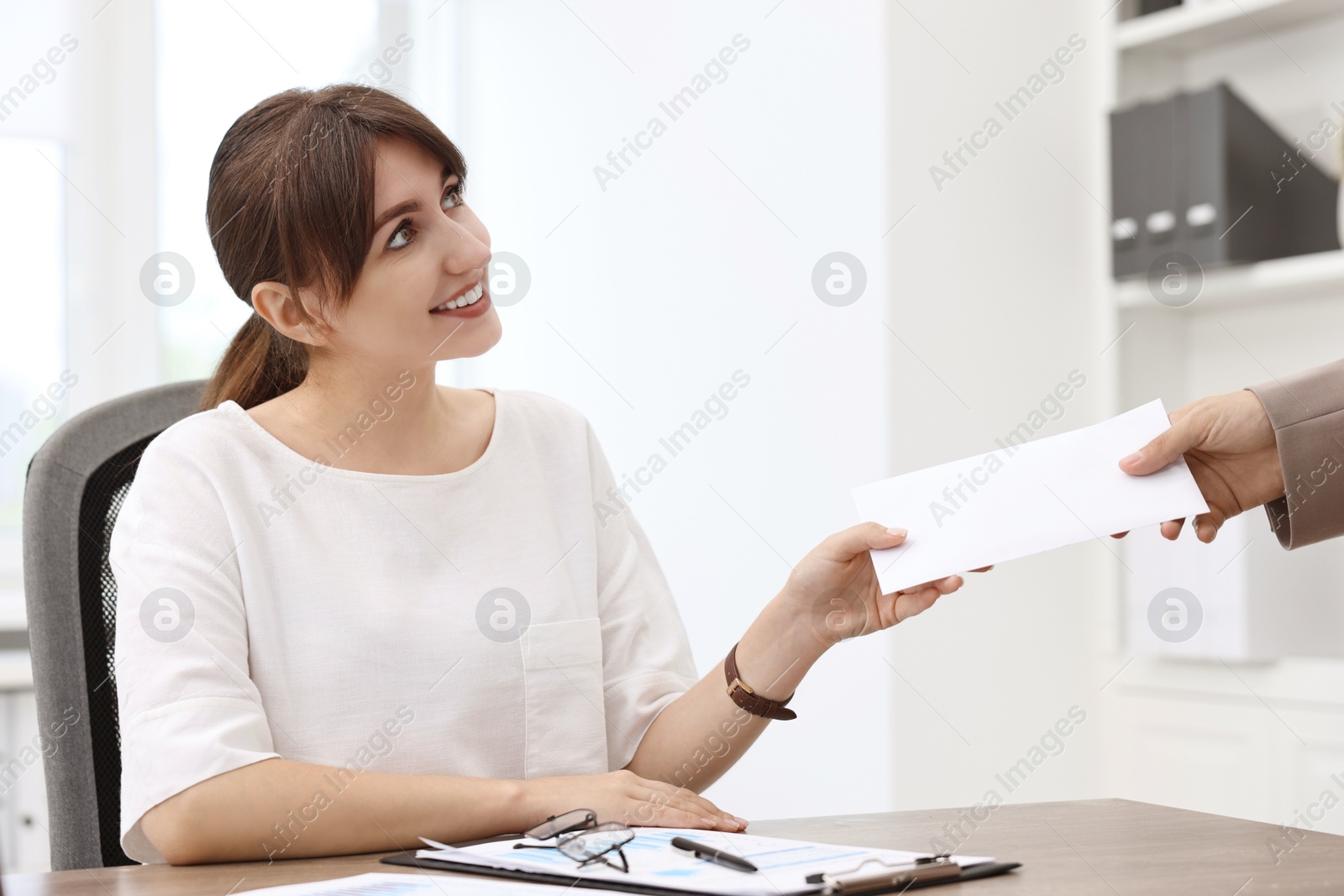 Photo of Smiling employee receiving envelope with salary from boss in office