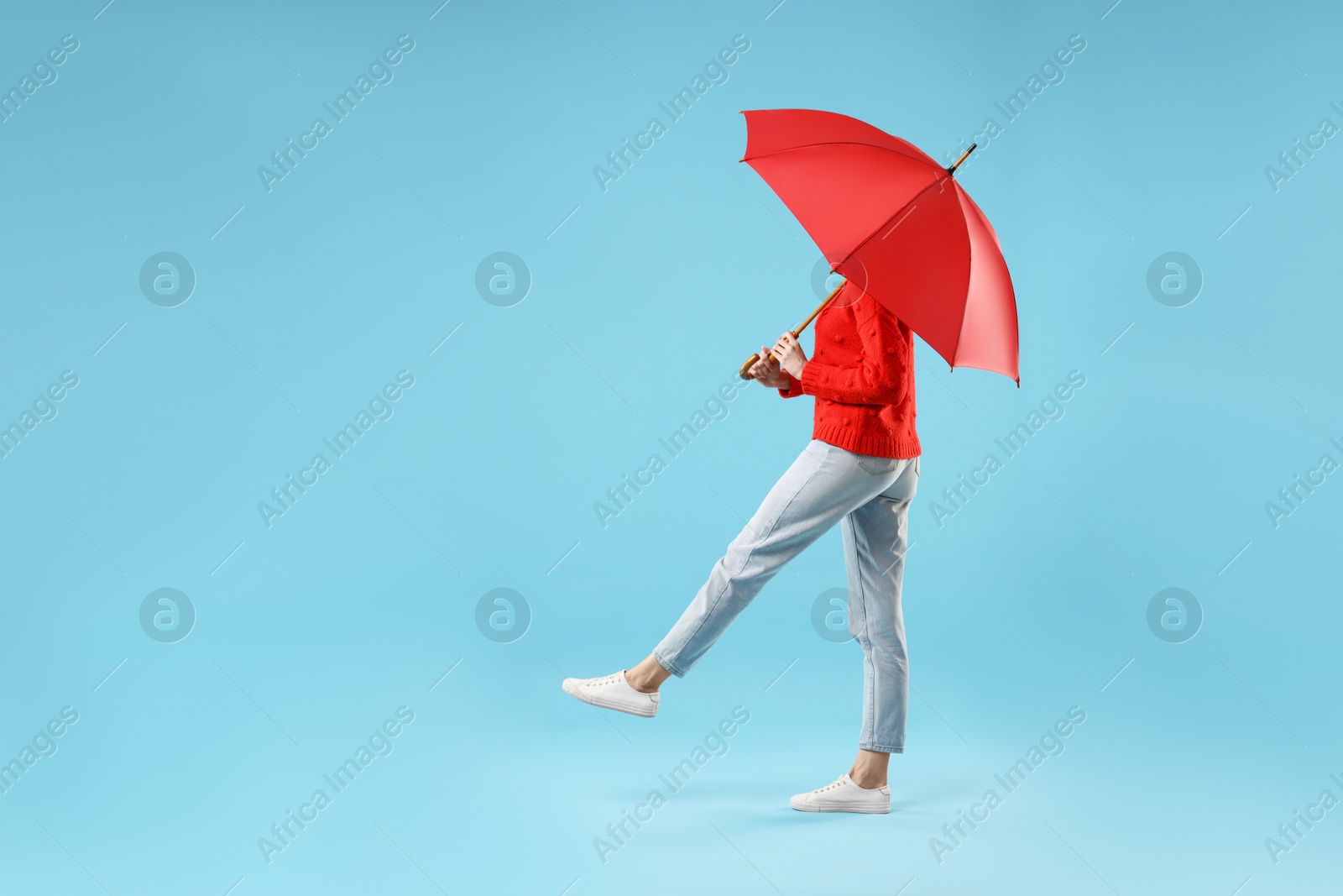 Photo of Woman with red umbrella walking on light blue background, space for text