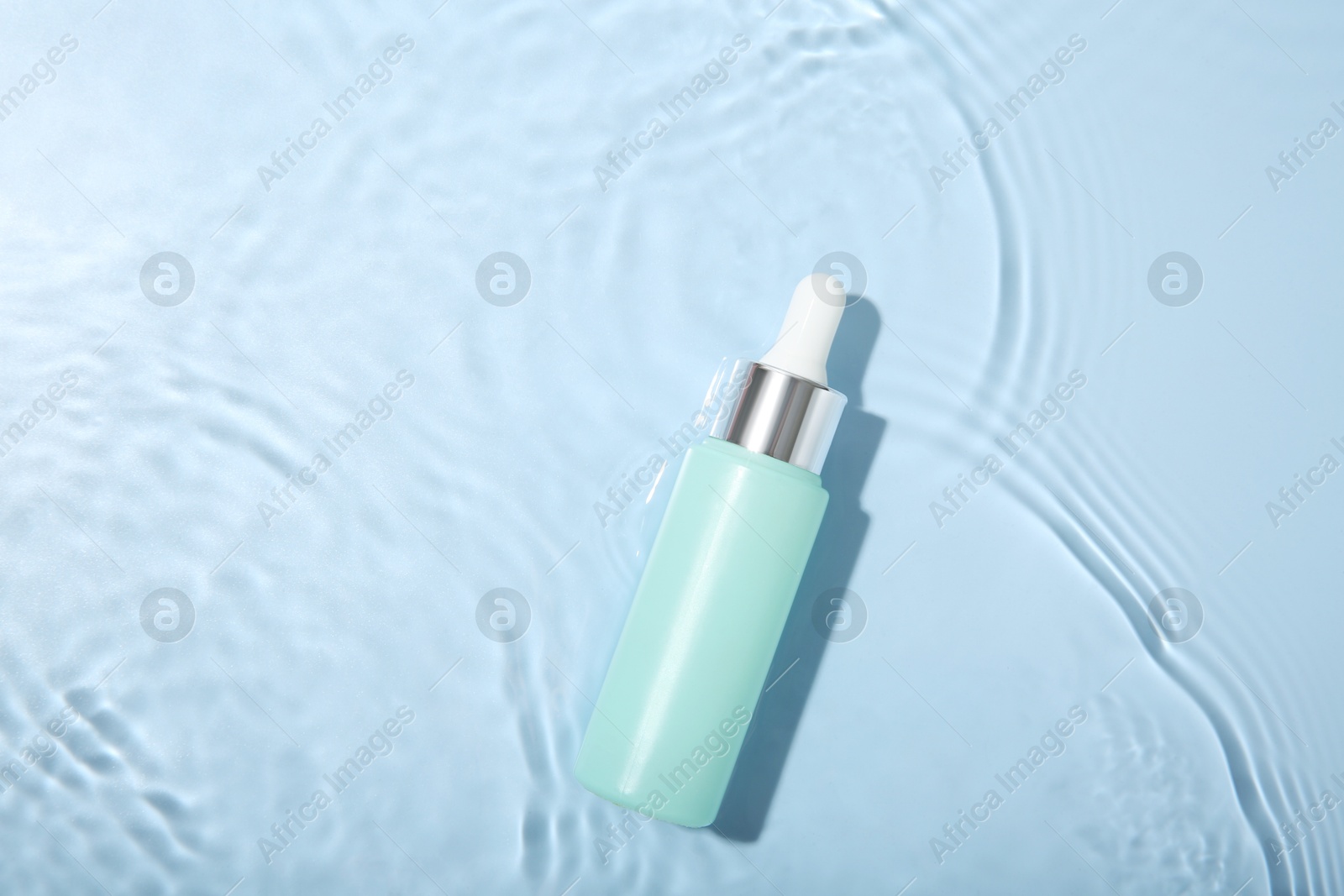 Photo of Bottle of cosmetic product in water on light blue background, top view