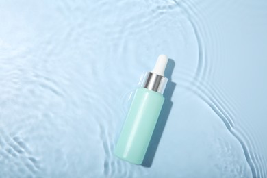 Photo of Bottle of cosmetic product in water on light blue background, top view