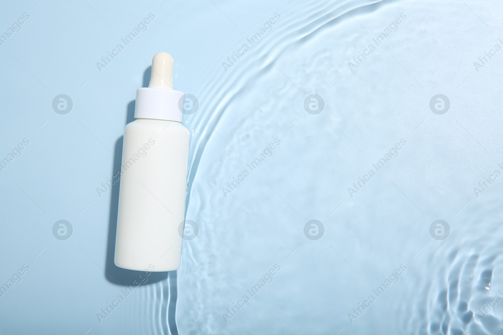 Photo of Bottle of cosmetic product in water on light blue background, top view. Space for text