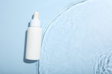 Bottle of cosmetic product in water on light blue background, top view. Space for text