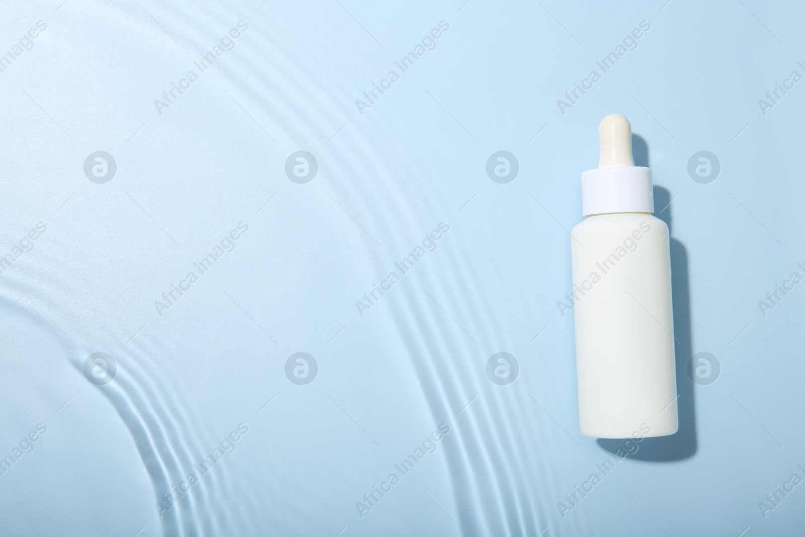 Photo of Bottle of cosmetic product in water on light blue background, top view. Space for text