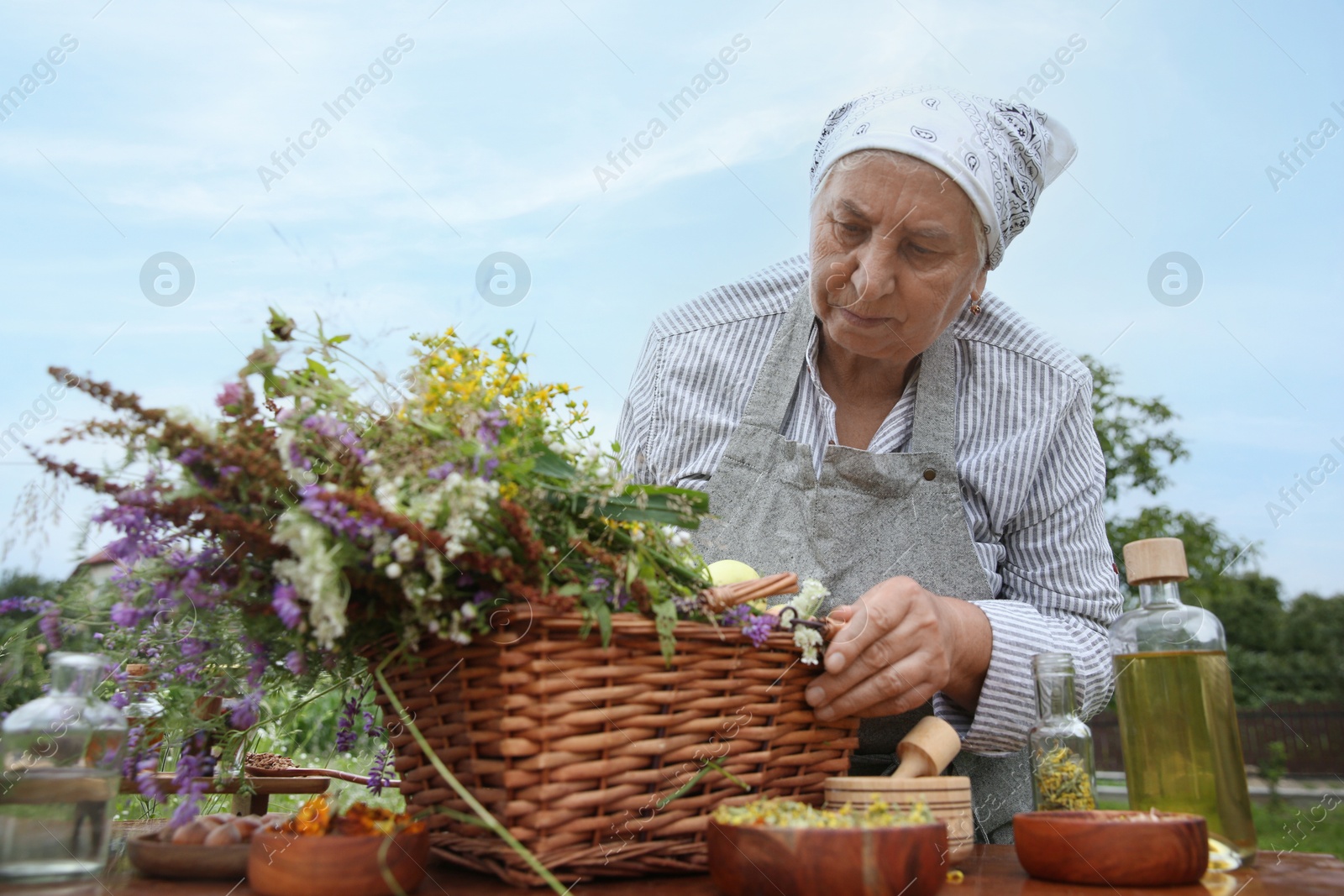 Photo of Senior woman with different ingredients for tincture outdoors