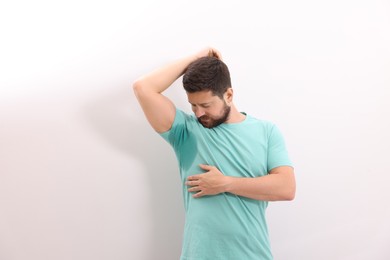 Emotional man in t-shirt before using deodorant on white background