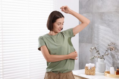 Photo of Emotional woman in t-shirt before using deodorant at home