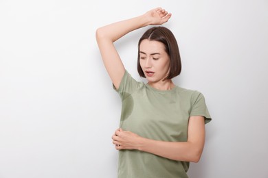 Emotional woman in t-shirt before using deodorant on white background