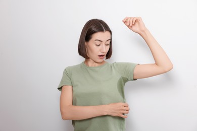 Emotional woman in t-shirt before using deodorant on white background