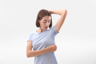 Emotional woman in t-shirt before using deodorant on white background