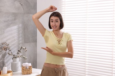 Photo of Emotional woman in t-shirt before using deodorant at home