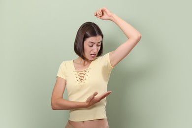 Emotional woman in t-shirt before using deodorant on green background