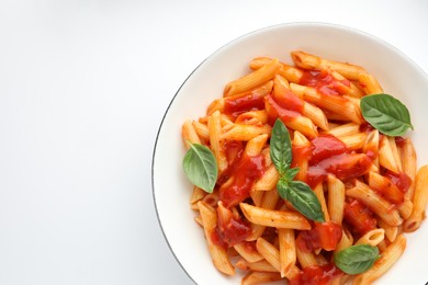 Delicious pasta with tomato sauce and basil in bowl on white background, top view. Space for text