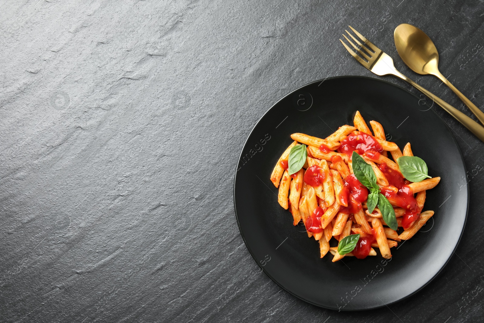 Photo of Delicious pasta with tomato sauce and basil served on black textured table, flat lay. Space for text