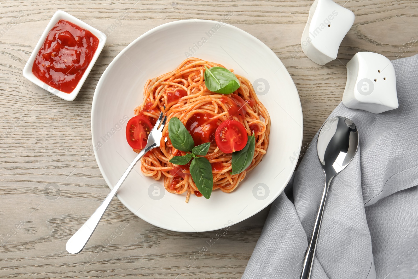 Photo of Delicious pasta with tomato sauce and basil in bowl served on wooden table, flat lay