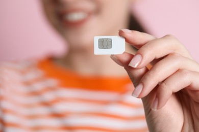 Woman holding SIM card on pink background, closeup