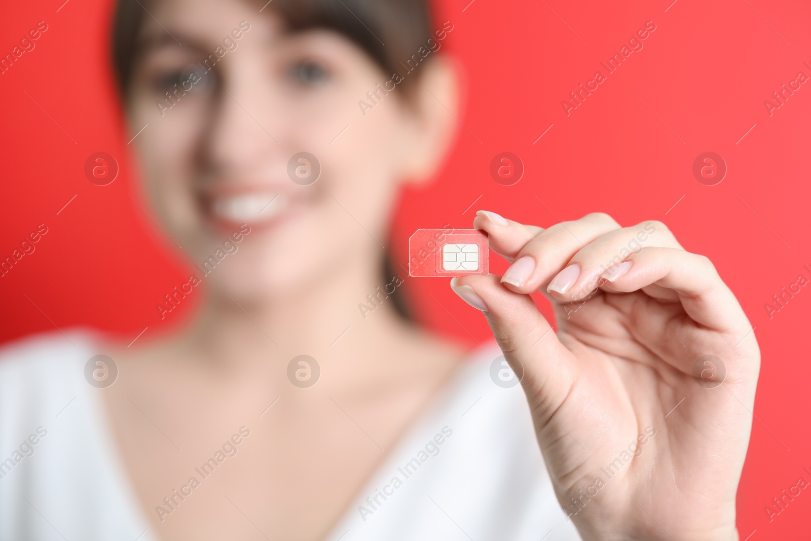 Photo of Woman holding SIM card on red background, selective focus