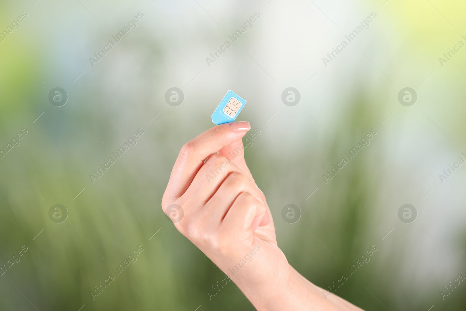 Photo of Woman holding SIM card on blurred background, closeup