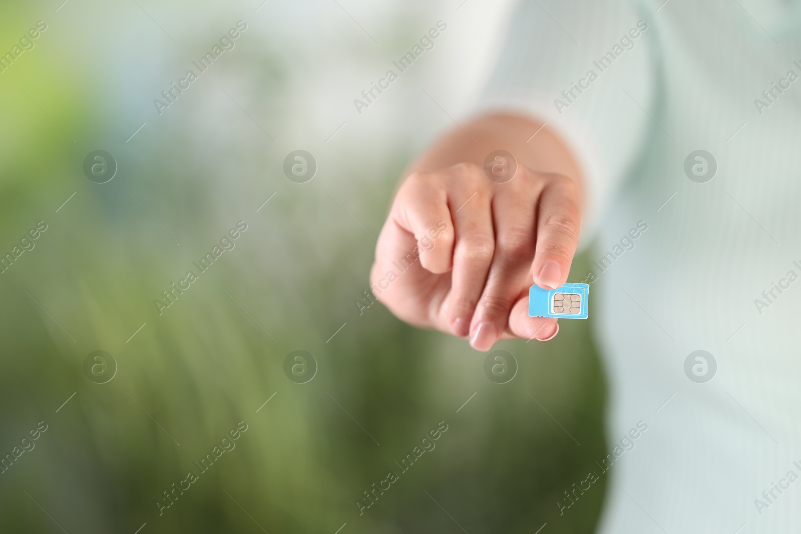 Photo of Woman holding SIM card on blurred background, closeup. Space for text