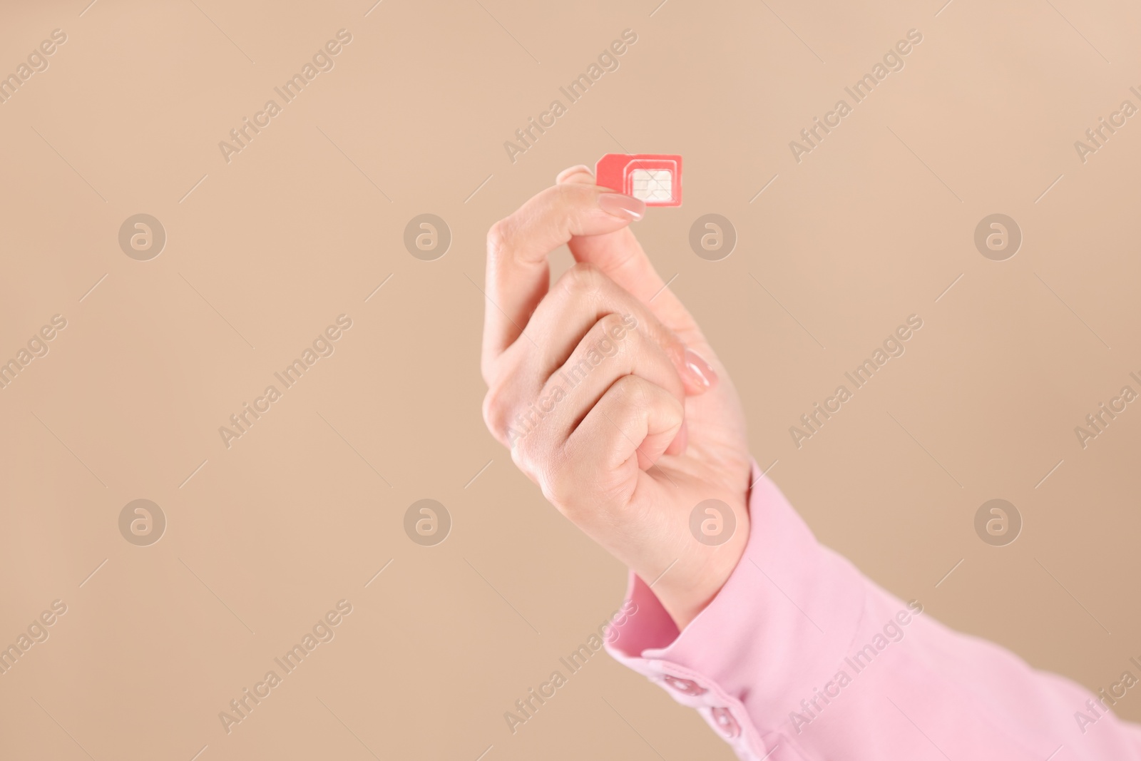 Photo of Woman holding SIM card on beige background, closeup. Space for text