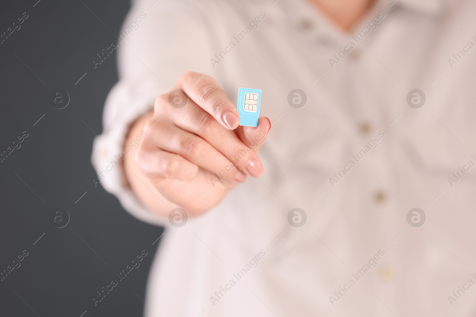 Photo of Woman holding SIM card on dark grey background, closeup