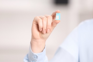 Photo of Woman holding modern SIM card indoors, closeup