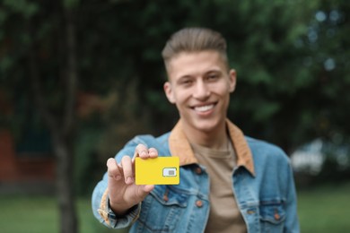 Happy man with SIM card outdoors, selective focus