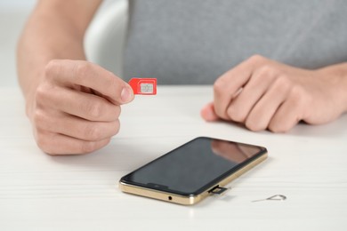 Photo of Man with SIM card near smartphone at white wooden table indoors, closeup