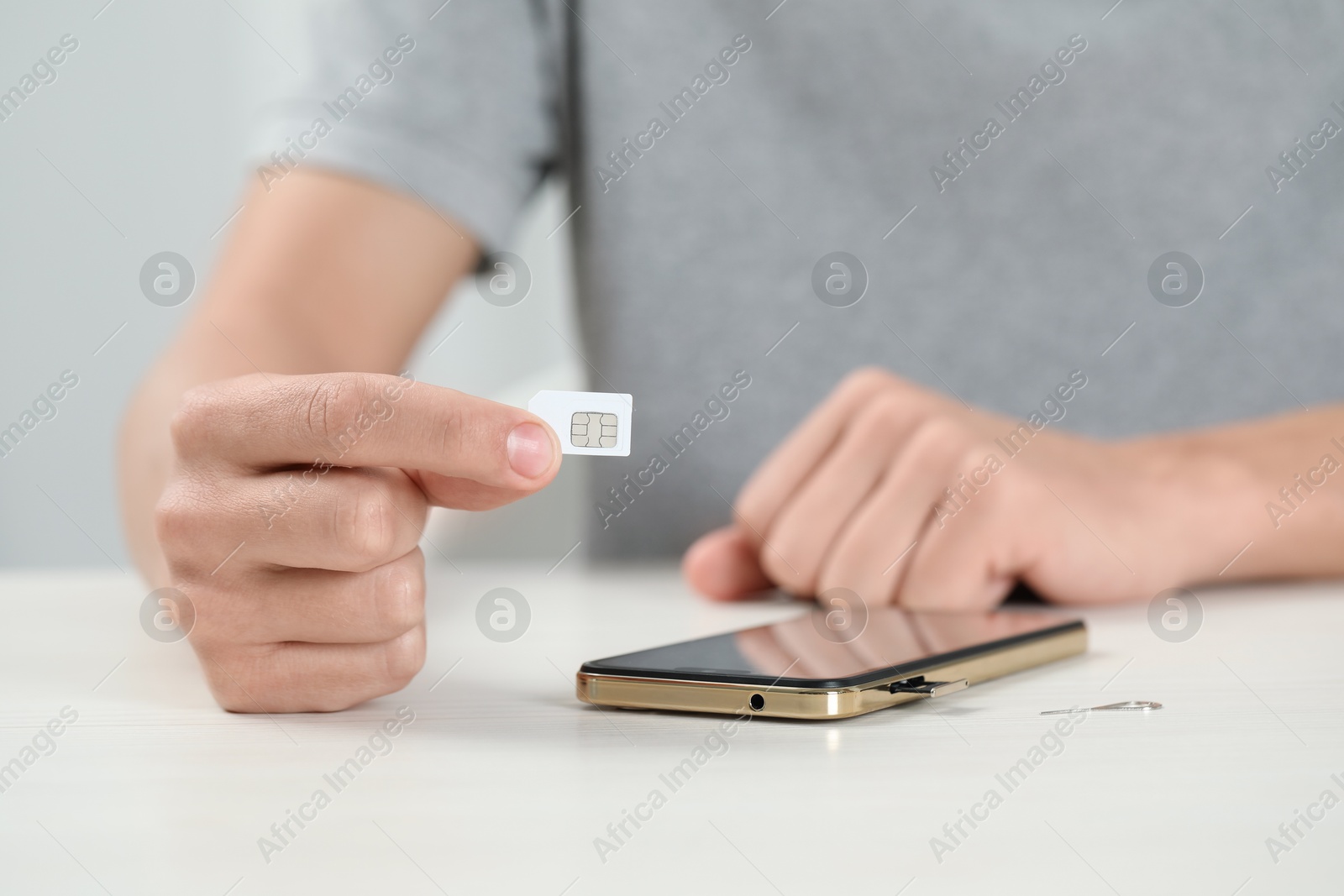 Photo of Man with SIM card near smartphone at white table indoors, closeup