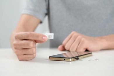 Man with SIM card near smartphone at white table indoors, closeup