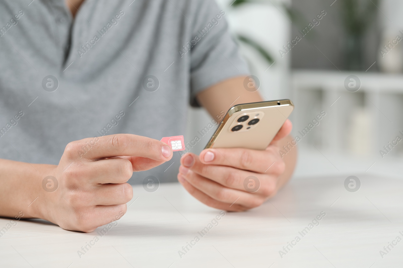 Photo of Man with SIM card and smartphone at white table indoors, closeup