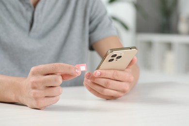 Man with SIM card and smartphone at white table indoors, closeup