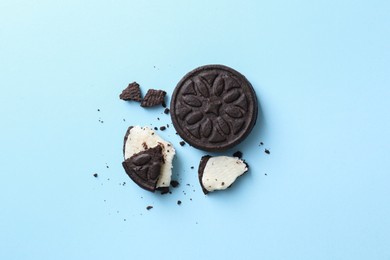 Whole and broken sandwich cookies on light blue background, top view