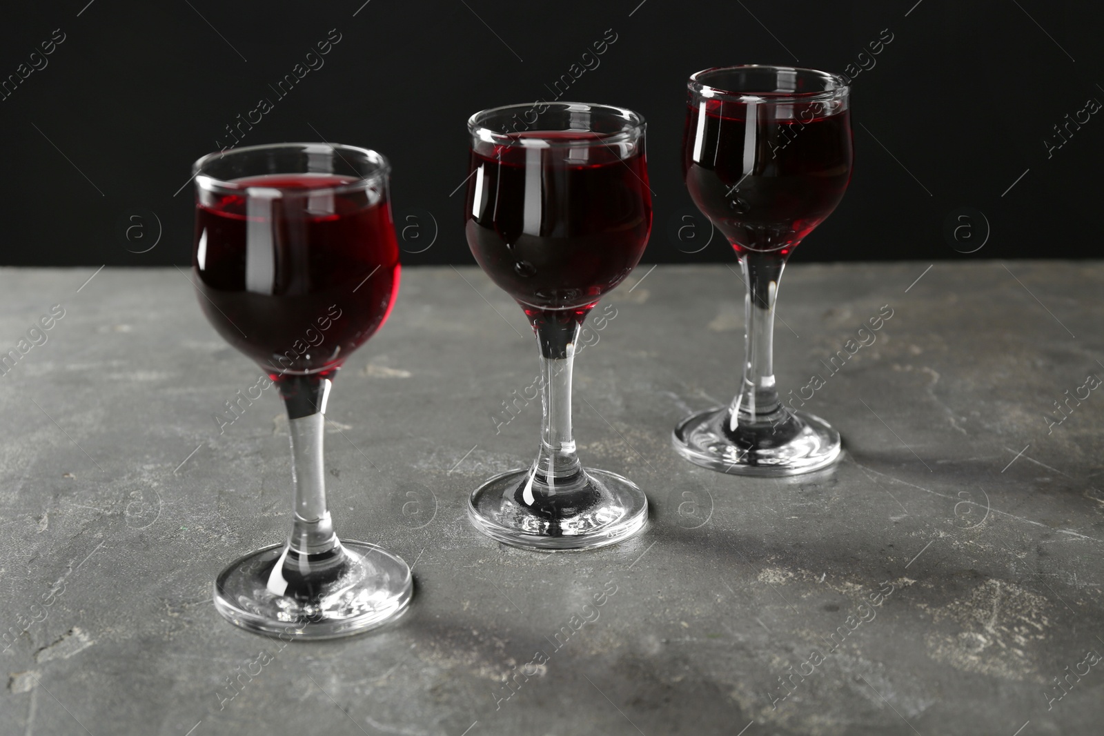 Photo of Delicious cherry liqueur in glasses on grey background