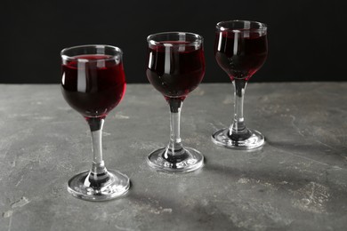 Delicious cherry liqueur in glasses on grey background