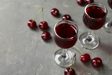 Photo of Delicious cherry liqueur in glasses and fresh berries on grey background, space for text