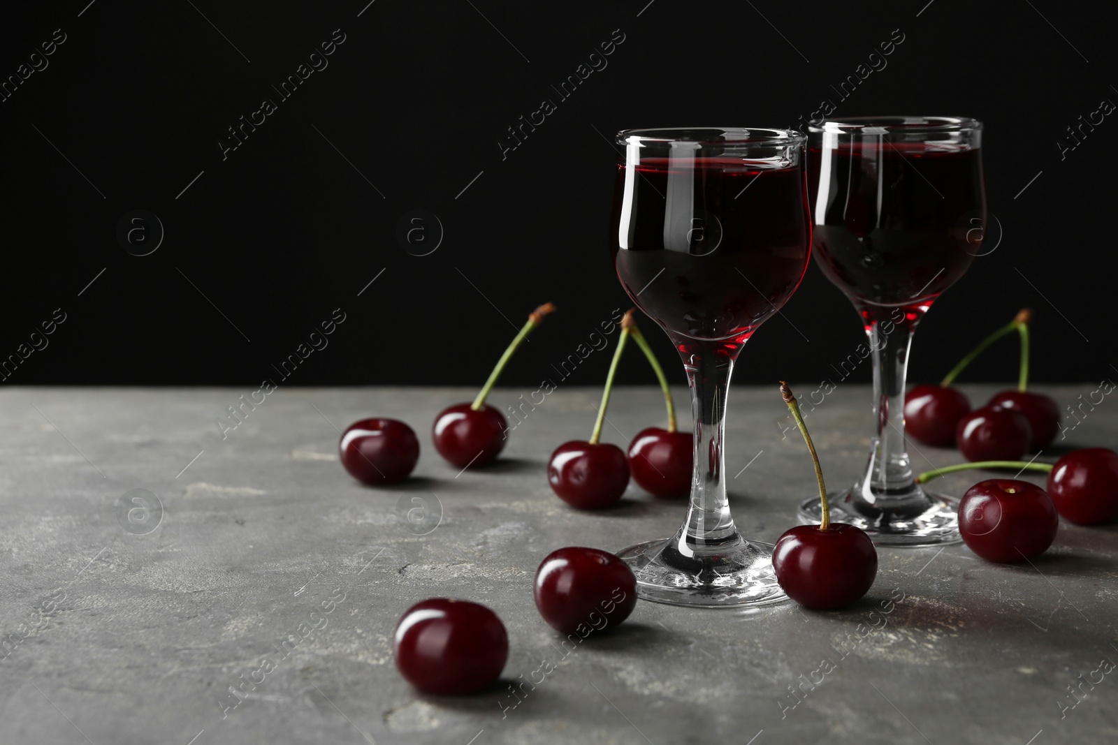 Photo of Delicious cherry liqueur in glasses and fresh berries on grey background, space for text