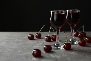 Photo of Delicious cherry liqueur in glasses and fresh berries on grey background, space for text