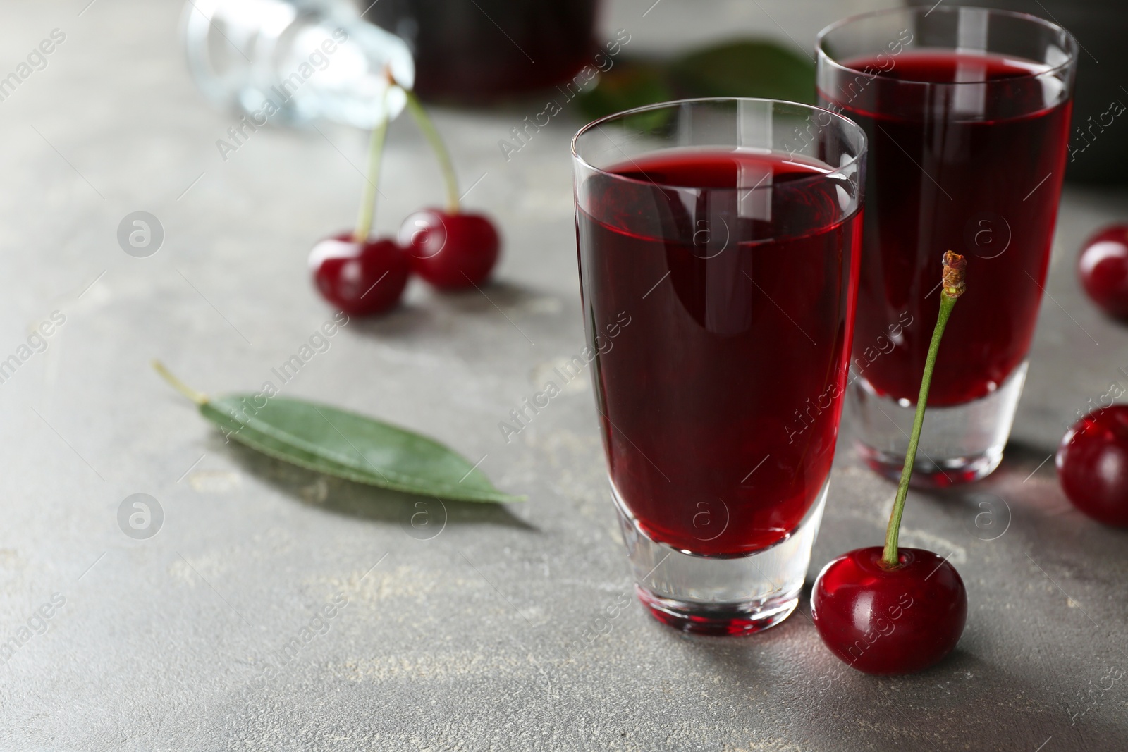 Photo of Delicious cherry liqueur in shot glasses and fresh berries on grey table, closeup