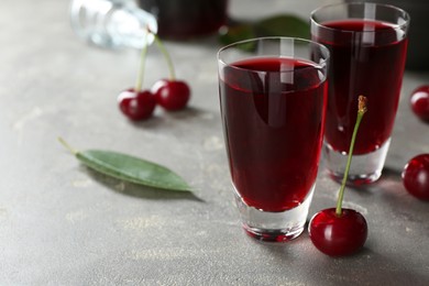 Delicious cherry liqueur in shot glasses and fresh berries on grey table, closeup