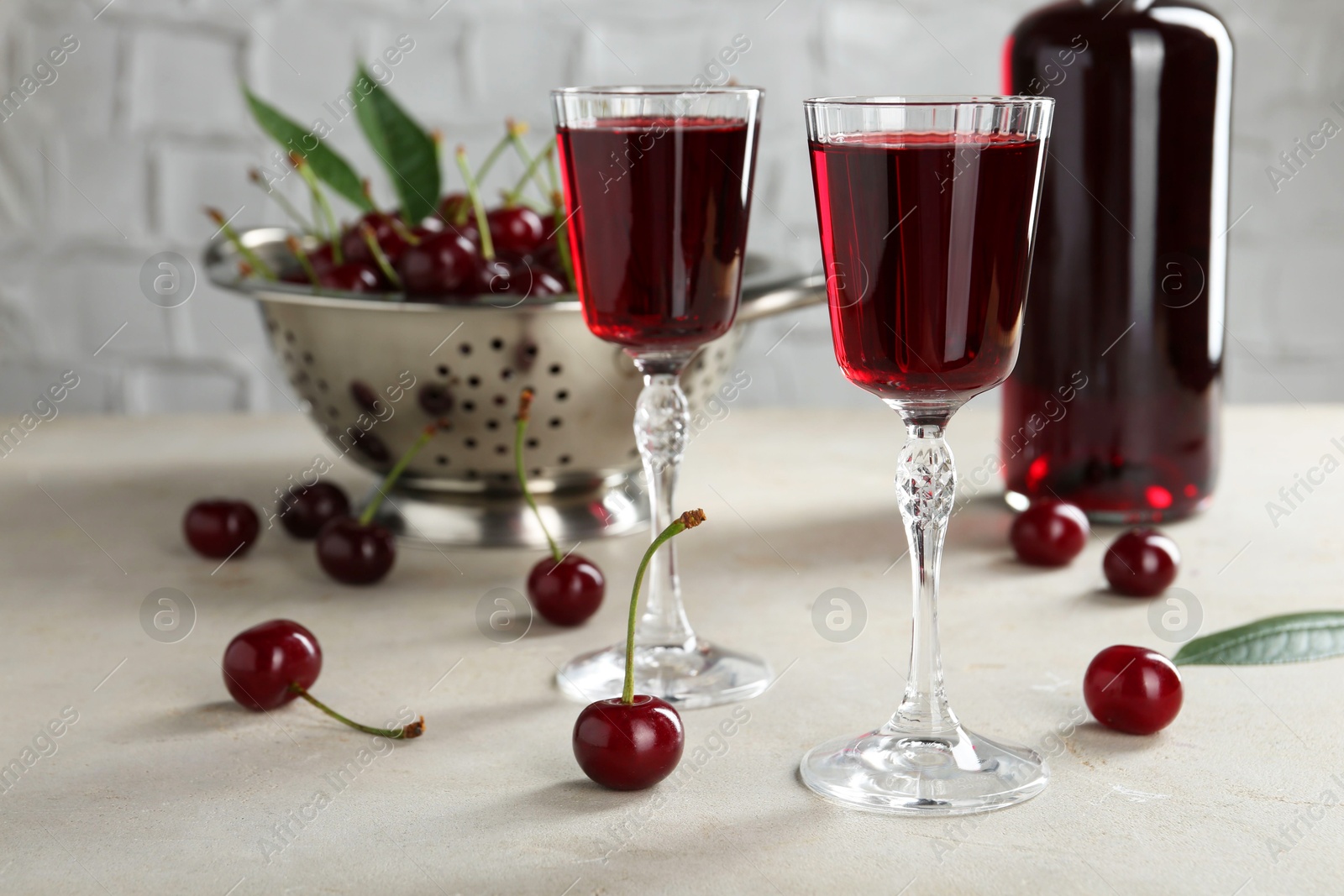 Photo of Delicious cherry liqueur in glasses and fresh berries on light grey table