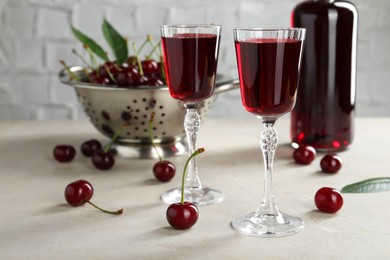 Delicious cherry liqueur in glasses and fresh berries on light grey table